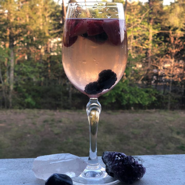 A glass of sangria with berries in it, surrounded by crystals on a balcony